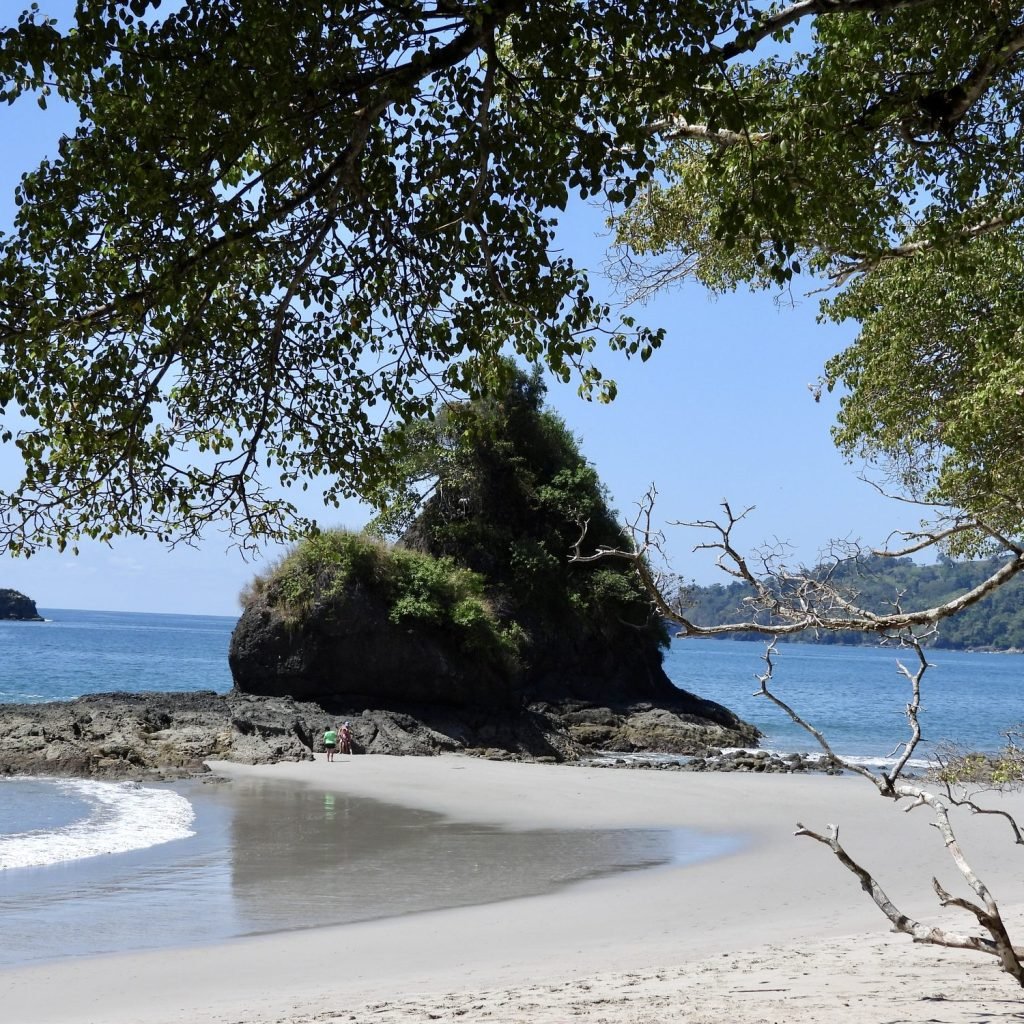 White sand beach in Manuel Antonio National Park with a forested rock outcrop rising from turquoise water